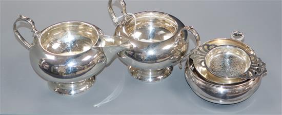 A modern silver cream jug and sugar bowl, a silver coaster, silver taste vin and silver tea strainer on stand.